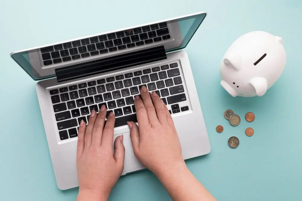 Persona tecleando en un portátil junto a una hucha: solicitud de minicrédito online
